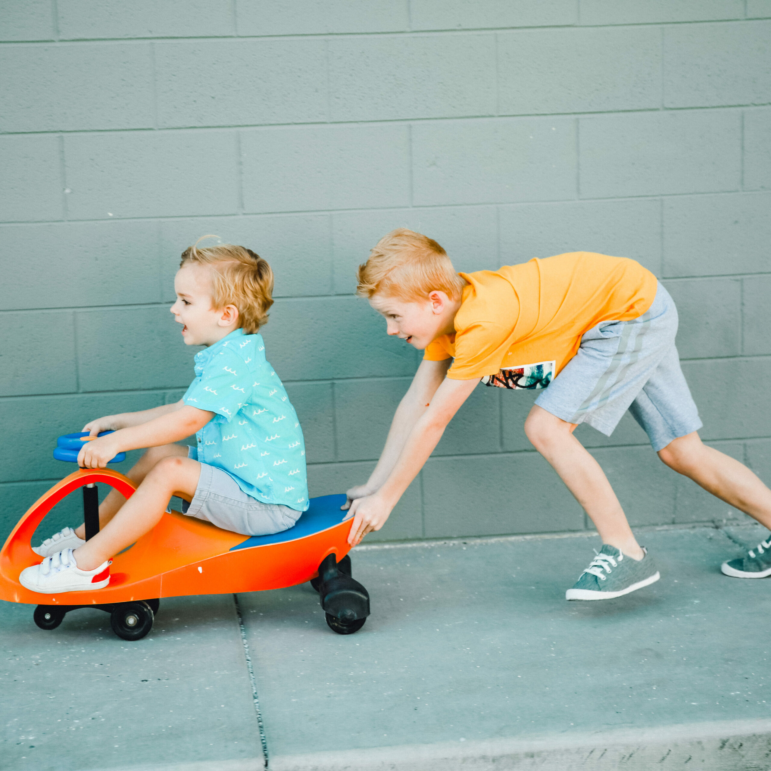 old boy pushing a younger boy on a toddler bike