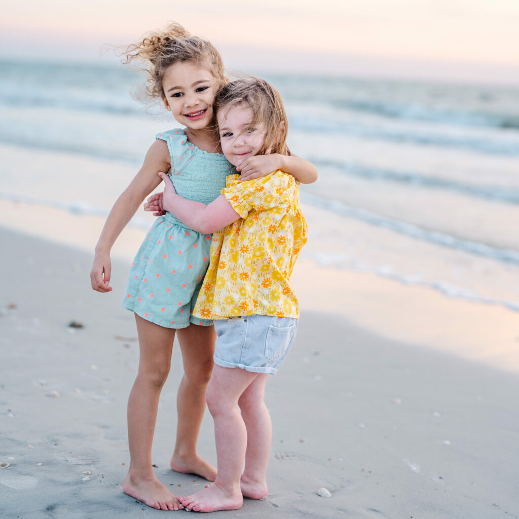 two girls hugging on the beach in summer clothes from kid to kid