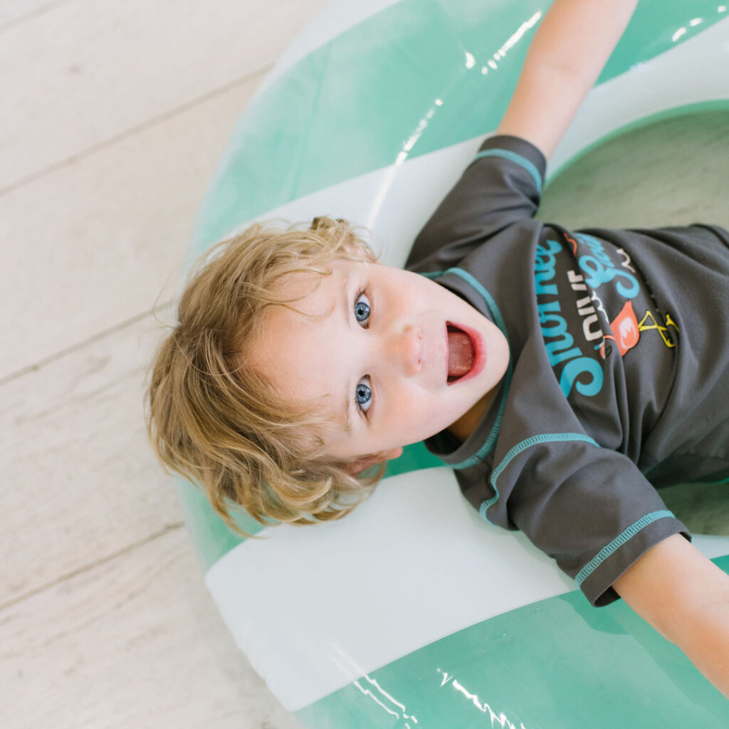 boy in swimwear sitting on a pool toy