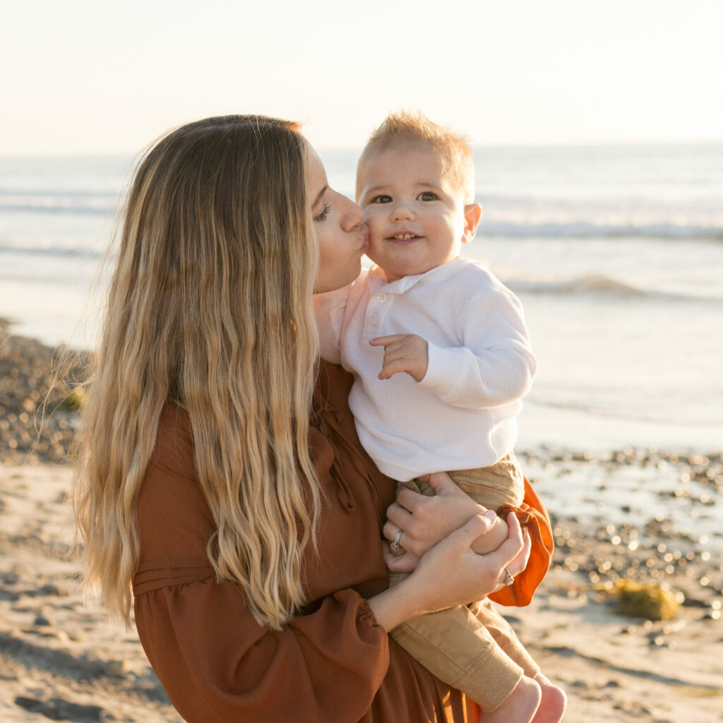 mother kissing her young sons cheek while she holds him on the sea shore