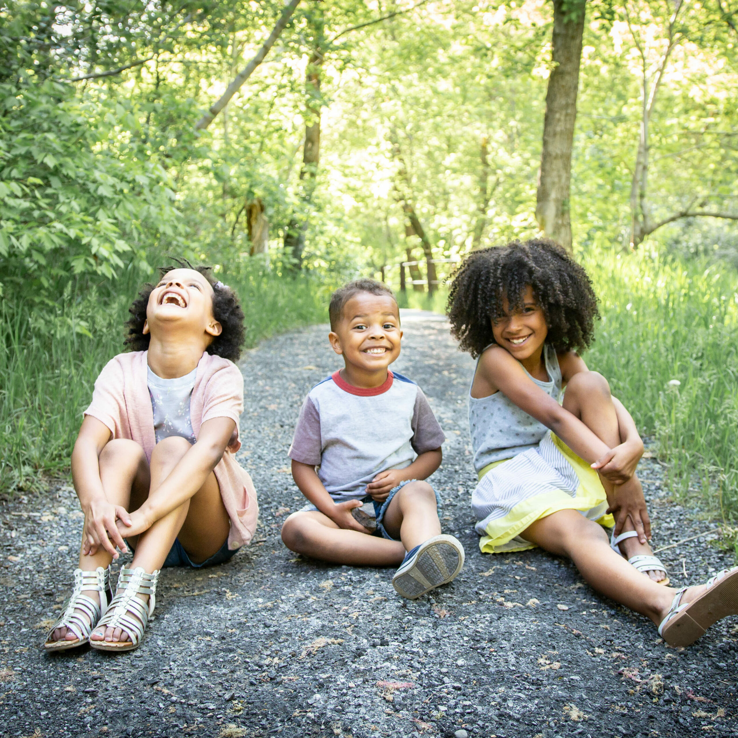 Three children sitting on the ground outside in the forest