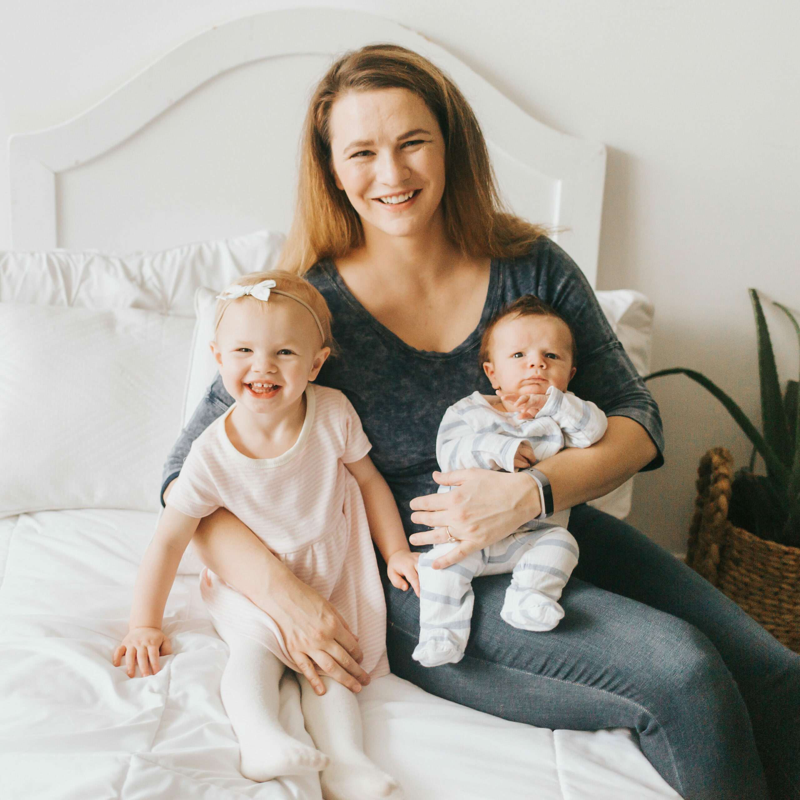 Mom sitting on a bed holding a toddler and an infant