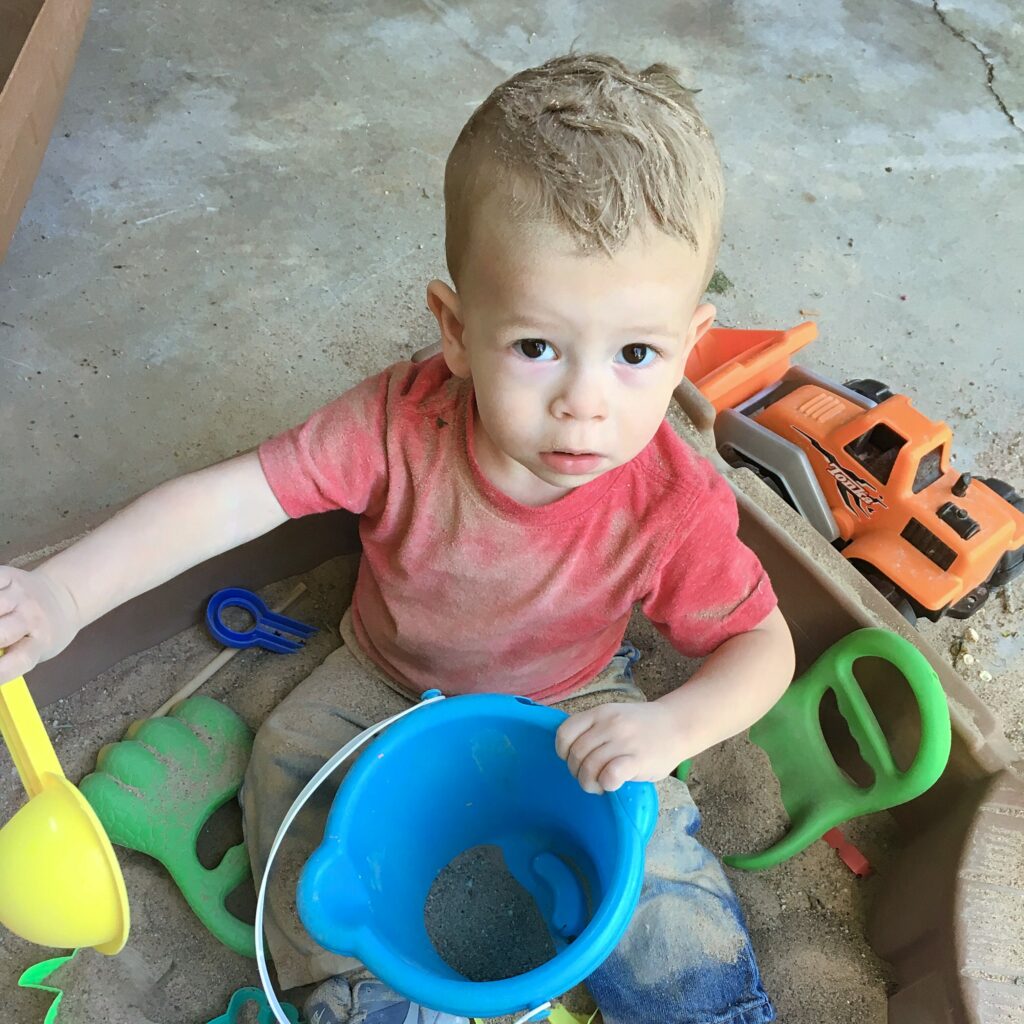 boy in sandbox covered in sand with toys from kid to kid