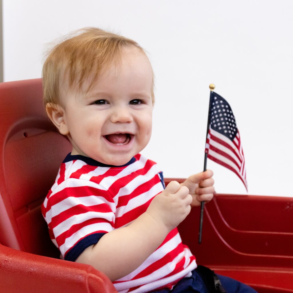 baby boy in a wagon holding the American flag