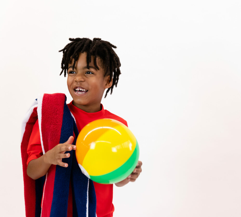 boy in swim gear from kid to kid holding a beach ball